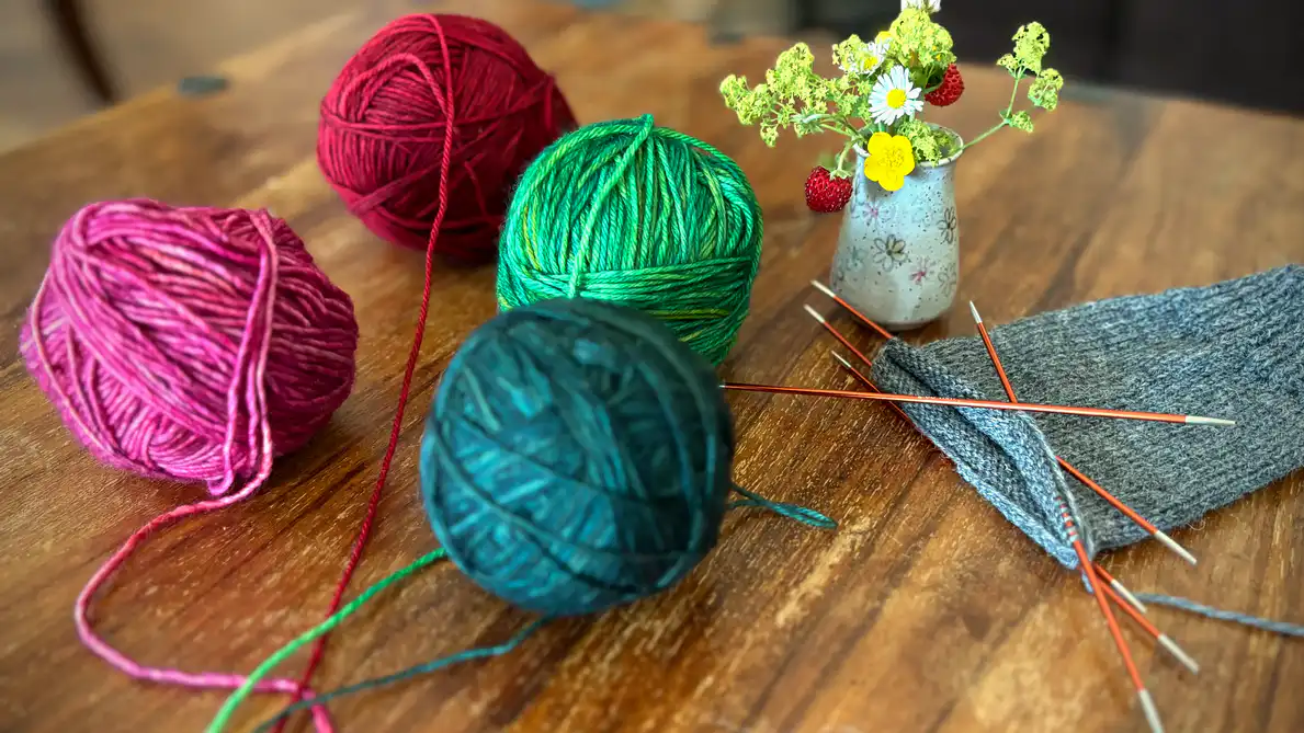 Bunte Wollknäule und Socke in Arbeit liegen auf dem Tisch
